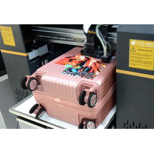 Pink suitcase with a colourful design being printed by on an Artisjet Trust UV printer